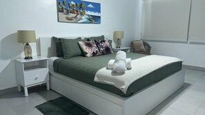 Ein ordentlich eingerichtetes Schlafzimmer mit einem Bett, zwei Nachttischen, einem Sessel und einem Bild an der Wand.