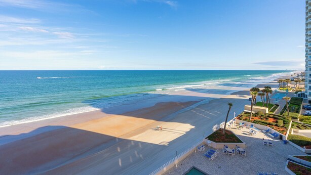 Ein Hotel direkt am Strand mit Blick auf das Meer, einem Poolbereich und einer Terrasse mit Sitzgelegenheiten.