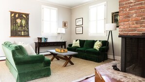 Ein Wohnzimmer mit grünen Sofas, einem Couchtisch, einem Kamin und gerahmten Kunstwerken an den Wänden.