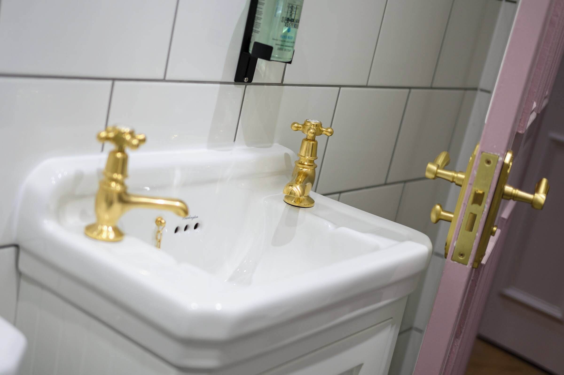 Ein Badezimmer mit einem weißen Waschbecken, zwei goldenen Wasserhähnen und einer rosafarbenen Tür.