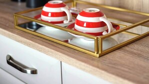A kitchen counter with a tray holding two red and white teapots, a white vase, and a black coffee maker. - Deluxe Double with Courtyard View (Room 4 - Lower Ground Floor) (Edinburgh)