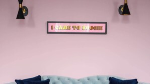 Un sofá celeste con tapicería capitonada y cojines azul oscuro, una pared rosa y un letrero enmarcado que dice "I CAME TO BOOGIE".