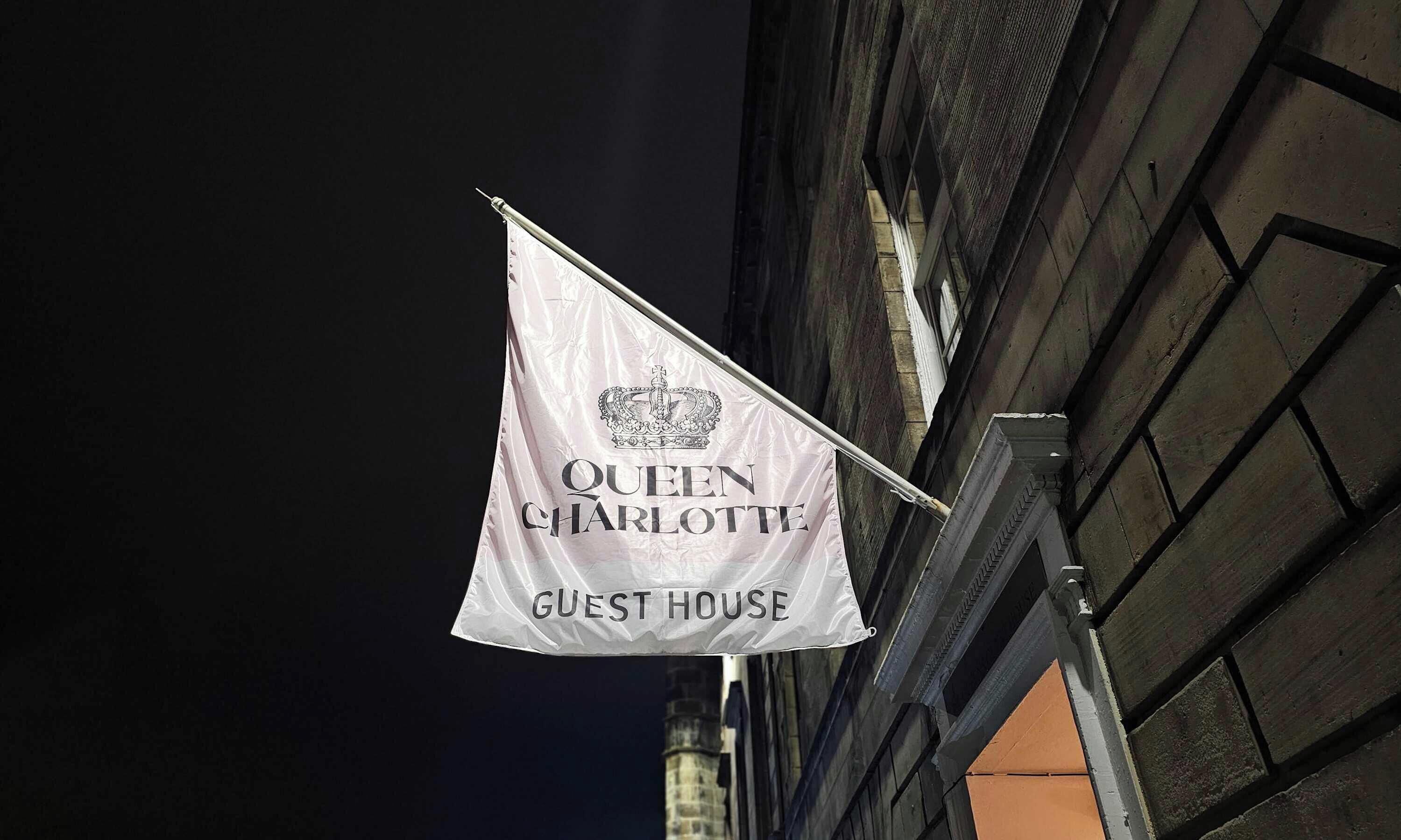 Eine Flagge mit dem Text "QUEEN CHARLOTTE GUEST HOUSE" und einem Wappen mit Krone.