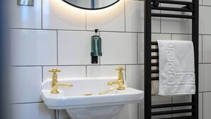 A bathroom with a white pedestal sink, gold faucets, a black towel rack, and a soap dispenser. - Deluxe Double Room (Room 10 - Ground Floor) (Edinburgh)