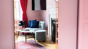 A room with a sofa, ottoman, table, and a fireplace. - Deluxe Family Room (Room 12 - First Floor) (Edinburgh)