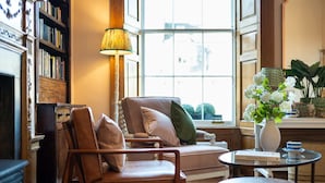 A cozy living room with a leather armchair, a sofa, a small round table, and a bookshelf. - Triple Room with Private Bathroom (2nd Floor - Room 7) (Edinburgh)