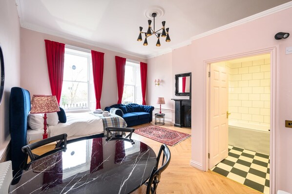Een hotelkamer met een bed, een blauwe bank, een eettafel en een open haard.