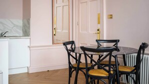 A dining area with a round table and four chairs, a white door with a gold handle, and a marble backsplash in the kitchen area. - Deluxe Family Room (Room 1 - Ground Floor) (Edinburgh)