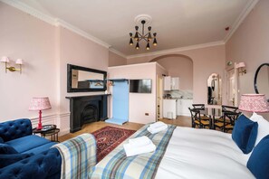 Een hotelkamer met een bed, twee fauteuils, een open haard, een televisie en een zithoek met een tafel en stoelen.