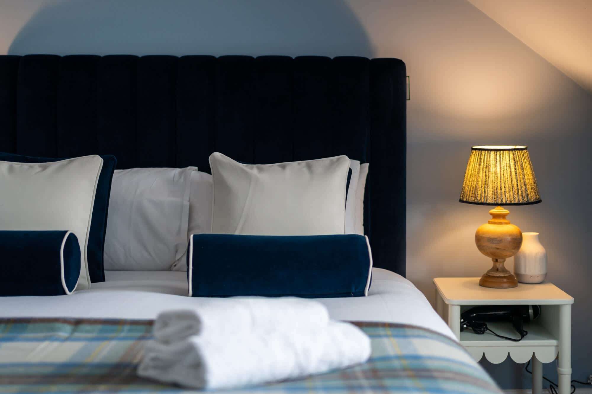 Un lit bien fait, avec une literie blanche et bleue, une lampe de chevet et une petite table de nuit avec une lampe.