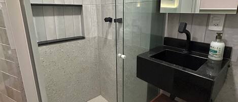 A modern bathroom with a glass shower enclosure, a black sink, and a mirror above it.