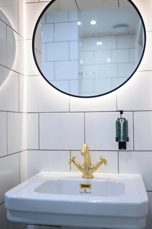A bathroom with a white sink, gold faucet, and a round mirror. - Deluxe Family Room (Room 3 - Lower Ground Floor) (Edinburgh)