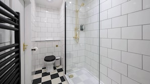 Une salle de bain moderne avec des carreaux blancs, un sol à carreaux noirs et blancs, une douche en verre et des toilettes avec un abattant noir.