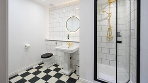 Um banheiro moderno com piso quadriculado preto e branco, vaso sanitário branco, pia de pedestal, espelho redondo e box de vidro.