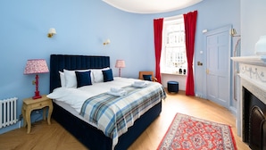 Quarto com cama, mesas de cabeceira, luminária vermelha e branca, cortina vermelha, lareira e janela com cortinas vermelhas.