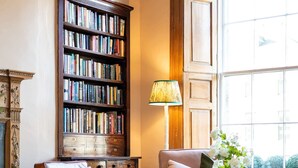 A cozy living room with a leather armchair, a sofa, a bookshelf, a lamp, and a window with a view. - Deluxe Double Room with Shower (3rd Floor - Room 12) (Edinburgh)