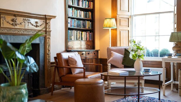 A cozy library with leather armchairs, a fireplace, a bookshelf, and a table with books and a vase of flowers. - Deluxe Double Room with Shower (3rd Floor - Room 12) (Edinburgh)