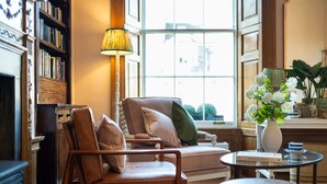A cozy living room with a leather armchair, a sofa, a small round table, and a bookshelf. - Deluxe Double Room with Shower (3rd Floor - Room 12) (Edinburgh)