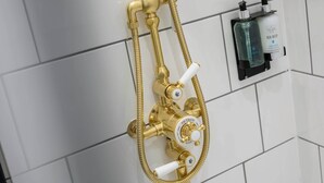 A gold showerhead with a control knob and a handheld shower attachment, mounted on a tiled wall. - Deluxe Family Room (Room 8 - Ground Floor) (Edinburgh)