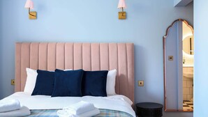 A neatly made bed with a pink headboard, two bedside lamps, and a round table beside it. - Deluxe Family Room (Room 8 - Ground Floor) (Edinburgh)
