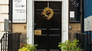 En svart dörr med en krans, en skylt med texten ”Angus Gordon Hairdressing & Beauty” och ett nummer 53 på byggnaden.