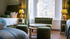 Ett hotellrum med en säng, två gröna fåtöljer, ett runt bord och två lampor.