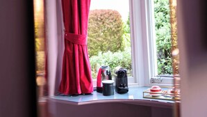 A room with a window, a mirror reflecting a red curtain, a small table with a kettle, and a blue stool. - Deluxe Double Room (Room 9 - Ground Floor) (Edinburgh)