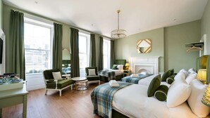 A hotel room with a large bed, two armchairs, a small table, a fireplace, and a view of the city through large windows. - Luxury Family Room with Private Bathroom (2nd Floor - Room 6) (Edinburgh)