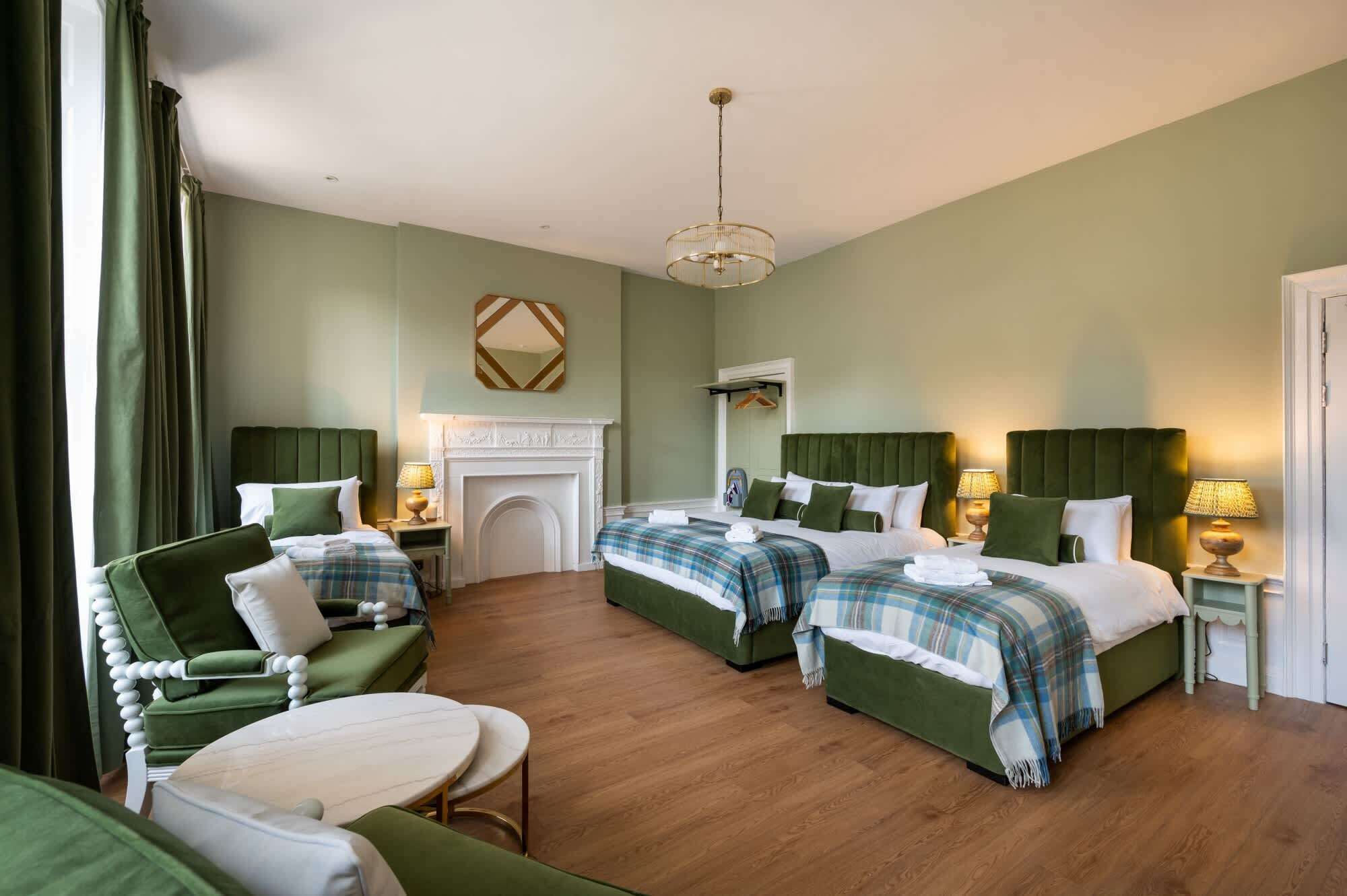 A hotel room with two beds, a fireplace, a round table, and a green armchair.