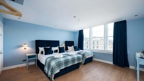 Una habitación de hotel moderna con una cama grande, dos mesitas de noche, un escritorio y vistas a la ciudad desde la ventana.