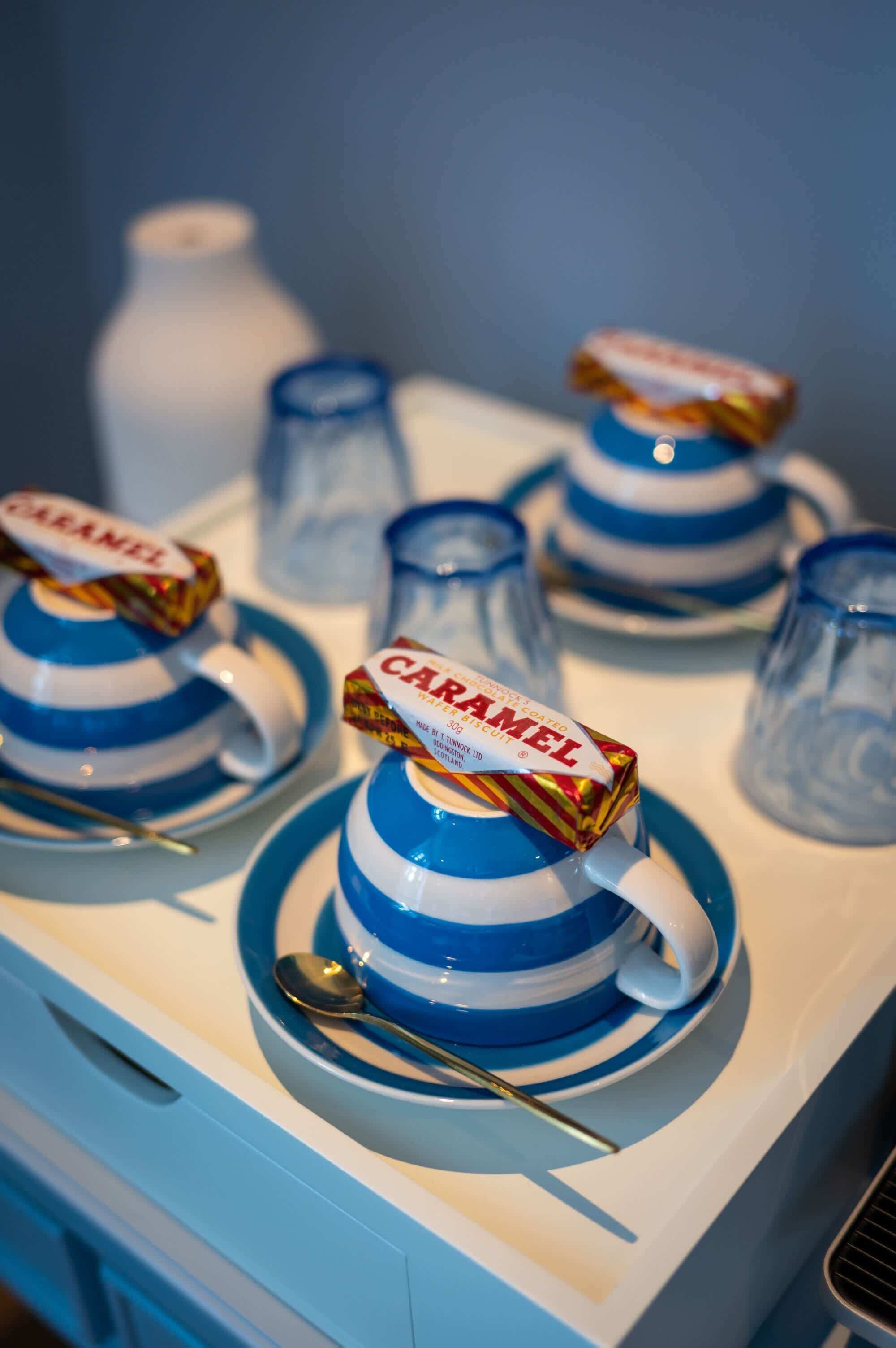 A table with blue and white striped cups and saucers, each topped with a caramel-colored candy wrapper.