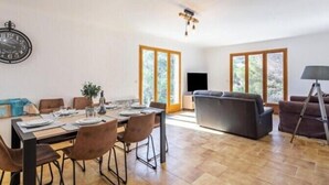 En rummelig opholdsstue med spisebord til fire personer, en sofa og et fjernsyn.