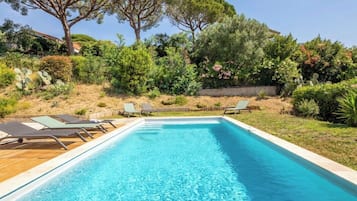 A rectangular swimming pool with clear blue water, surrounded by a wooden deck with lounge chairs.