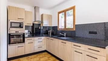 A modern kitchen with wooden cabinets, a black countertop, a built-in oven, a microwave, a window, and a sink.