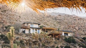 A modern two-story house with a balcony, situated on a rocky hillside with sparse vegetation. - High Point · 6-Acres, Sweeping Views, Hot Tub (Joshua Tree)