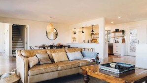 A spacious living room with a leather sofa, wooden coffee table, and a kitchen in the background. - High Point · 6-Acres, Sweeping Views, Hot Tub (Joshua Tree)