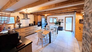Une cuisine moderne avec des poutres en bois, un coin repas doté d’une longue table et un mur en pierre.