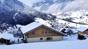 Un chalet en bois, doté d’un toit à pente, entouré de montagnes et d’arbres couverts de neige.