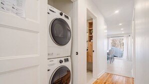 A laundry room with two Samsung washing machines, a wooden floor, and a view of a dining area with a table and chairs. - 2-bedroom condo in beautiful Montréal I Bright, Modern & Cozy (Montréal)