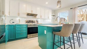 A modern kitchen with teal cabinetry, stainless steel appliances, and a bar area with two stools. - 2-bedroom condo in beautiful Montréal I Bright, Modern & Cozy (Montréal)