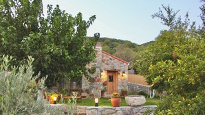 A stone cottage with a wooden door, surrounded by lush greenery and potted plants. - Detached Single - Storey Stone house in Datça Karaincir - Karaincir Houses 1 (Datça)