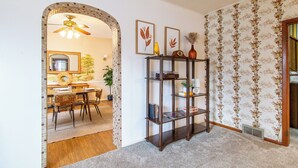 Een hal met houten vloer, betegelde muur, een boekenkast en een eethoek met een tafel en stoelen.