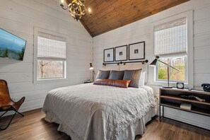Ein Schlafzimmer mit einem großen Bett, Holzboden und zwei Fenstern mit Jalousien.