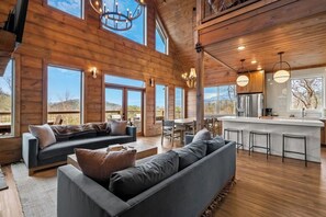 A spacious living area with a large sofa, a dining table, and a kitchen area with a bar. - Thunder Mountain Escape w/Private Indoor Pool (Sevierville)
