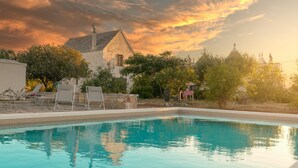 Une piscine avec des chaises longues, un bâtiment en pierre et des arbres en arrière-plan.