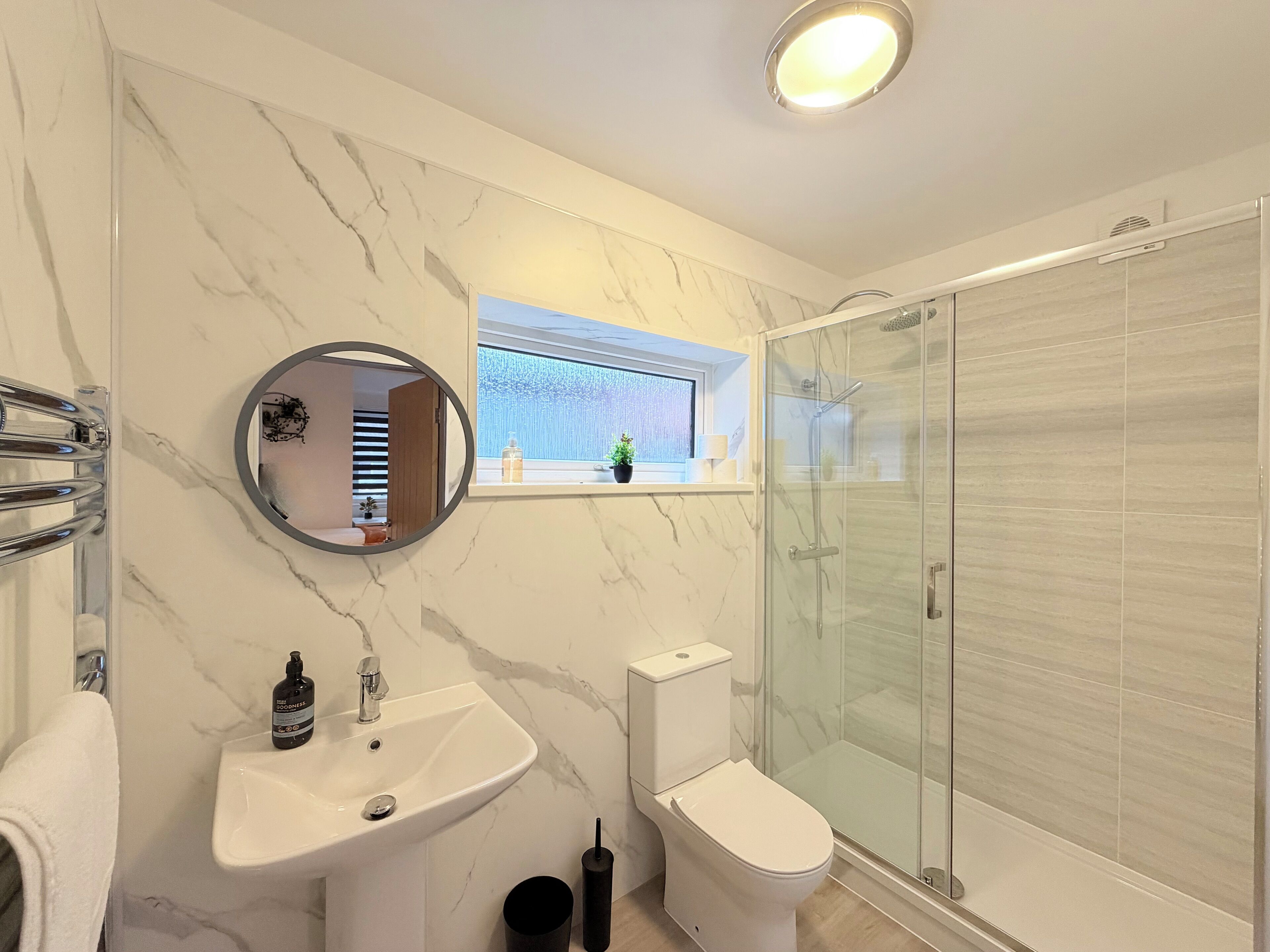 A modern bathroom with a marble backsplash, a round mirror, a sink, a toilet, and a glass-enclosed shower.