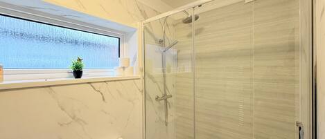 Une salle de bain avec une douche à parois de verre, des toilettes, une fenêtre avec une plante et des murs en marbre.