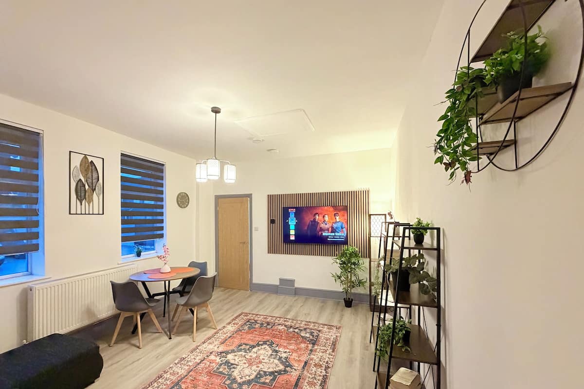 A modern living room with a dining area, a TV mounted on a wooden panel, and a staircase leading to another level.
