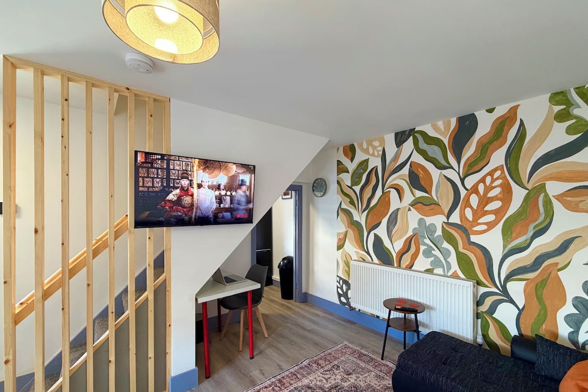 A modern living room with a TV, a sofa, a patterned wall, and a staircase.