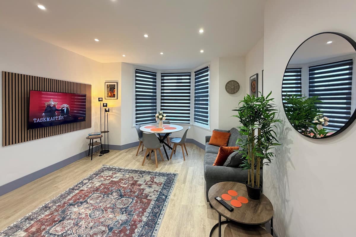 A modern living room with a TV, a dining table, a sofa, and a large mirror.